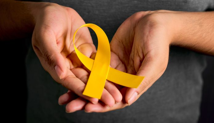 Photo showing hand holding a yellow ribbon for National Suicide Prevention Month