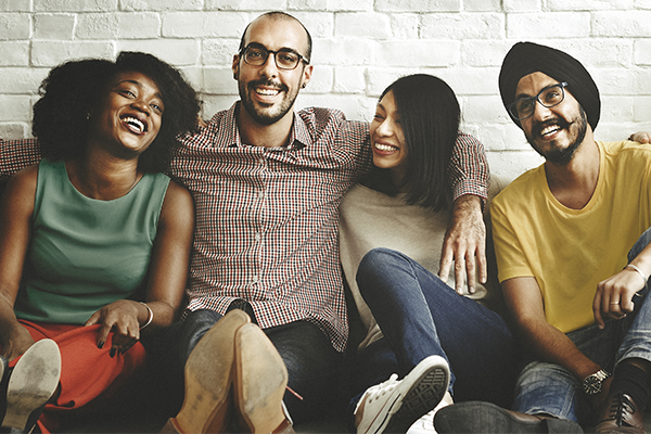 Photo showing group of four diverse people sitting on a couch and smiling